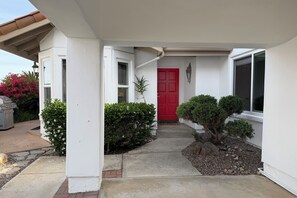 A residential entrance with a red door, a small garden with shrubs, and a barbecue grill outside. - Cute 2-bedroom Oceanside house in beautiful 55+ Ocean Hills Country Club (Oceanside)