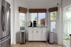 A modern kitchen with white cabinets, a stainless steel refrigerator, a coffee maker, and two trash bins. - Cute 2-bedroom Oceanside house in beautiful 55+ Ocean Hills Country Club (Oceanside)