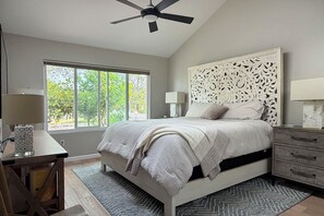 A bedroom with a bed, a desk, a chair, a ceiling fan, a window with a view of trees, and a nightstand with a lamp. - Cute 2-bedroom Oceanside house in beautiful 55+ Ocean Hills Country Club (Oceanside)
