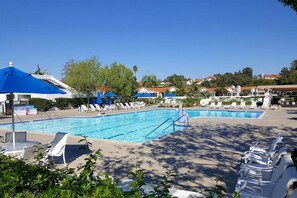 A swimming pool with lounge chairs and umbrellas, surrounded by greenery and buildings. - Cute 2-bedroom Oceanside house in beautiful 55+ Ocean Hills Country Club (Oceanside)
