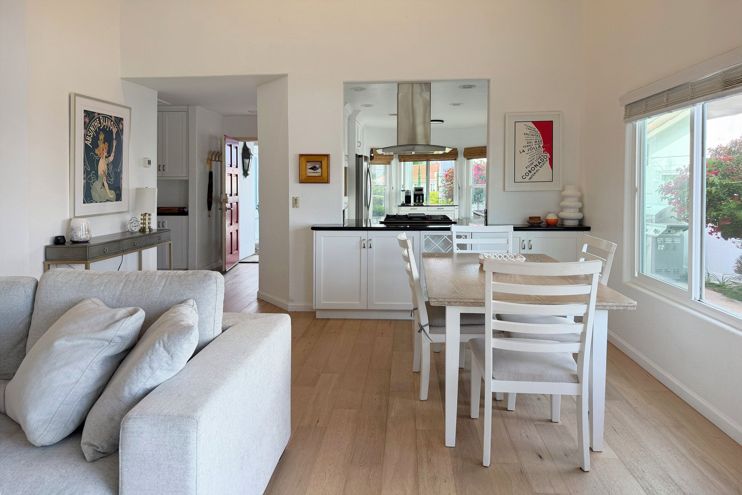 A modern kitchen with white cabinets, a dining table with white chairs, and a large window with a view of the outside.