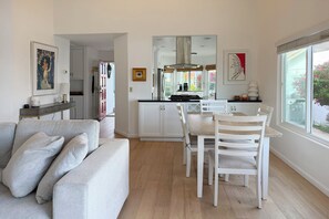 Eine moderne Küche mit weißen Schränken, einem Esstisch mit weißen Stühlen und einem großen Fenster mit Blick nach draußen.