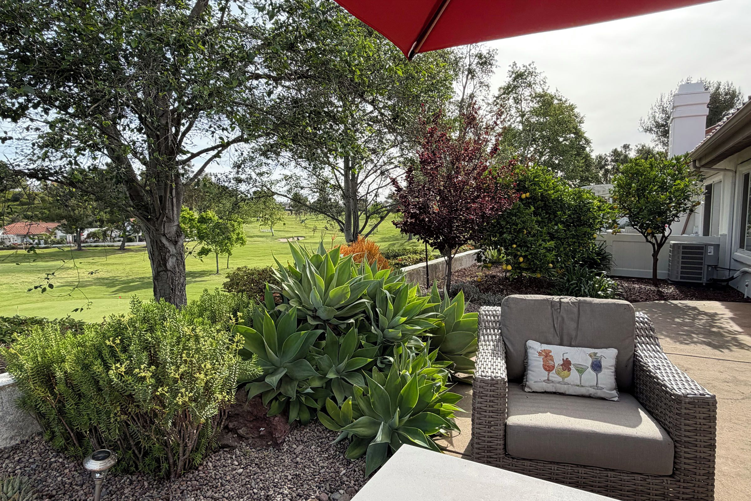 A patio area with a wicker chair, a red umbrella, and various plants.
