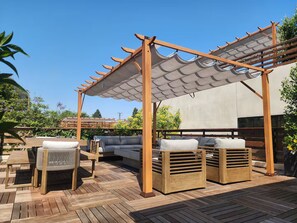 Eine Außenpatio mit Holzmöbeln, ein Gartenhaus mit beschattetem Bereich und Blick auf einen Garten.