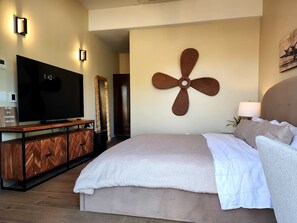 Ein modernes Schlafzimmer mit einem großen Bett, einem Flachbildfernseher, einer Holzkommode und einem Wandventilator.