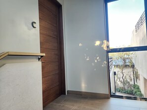 A hallway with a wooden door, a white wall, and a glass door leading to an outdoor area with plants. - Boutique Treetop Room at Jackson Market (Culver City)