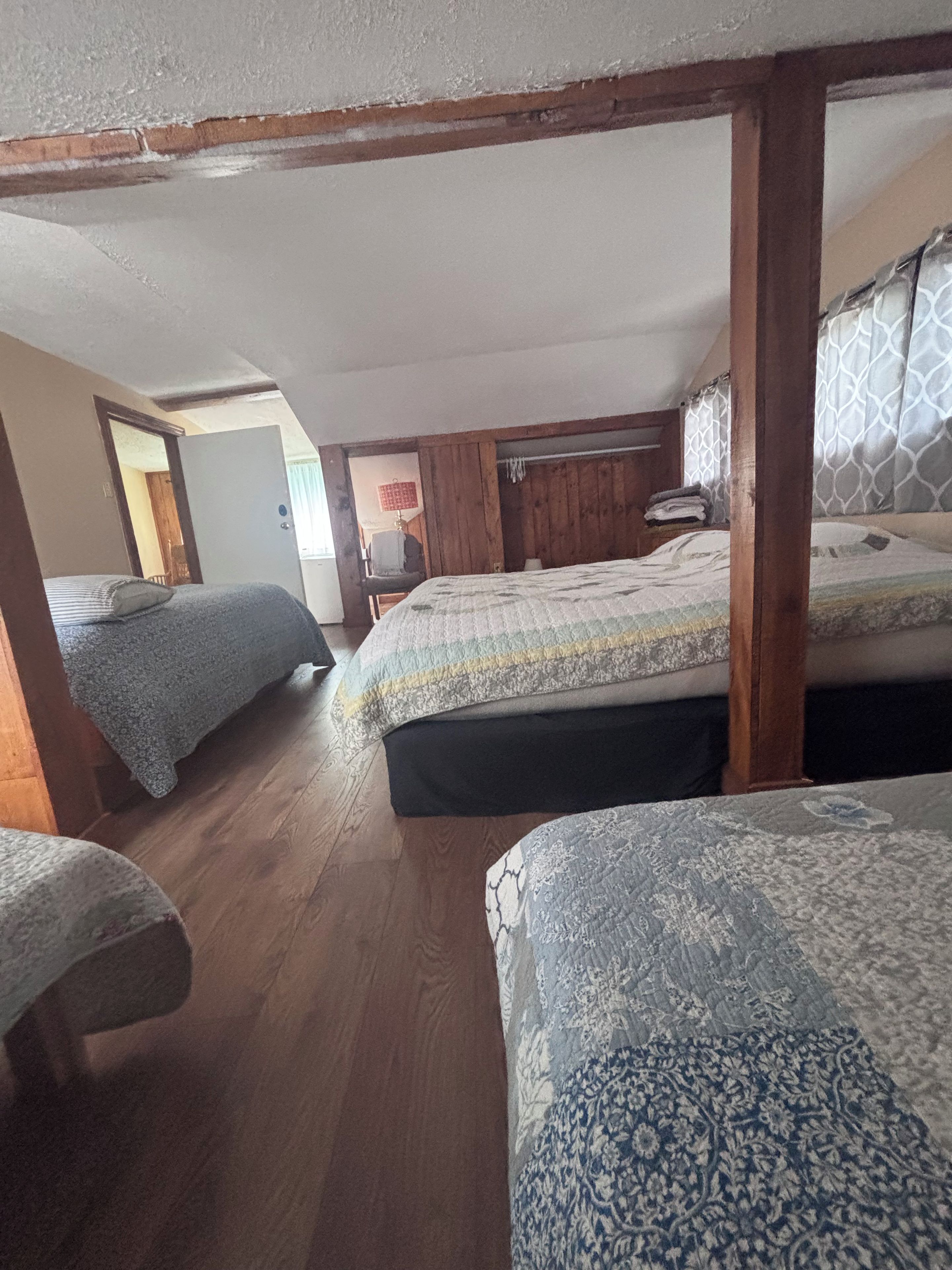 A room with two beds, wooden beams, a patterned rug, and a door leading to another room.