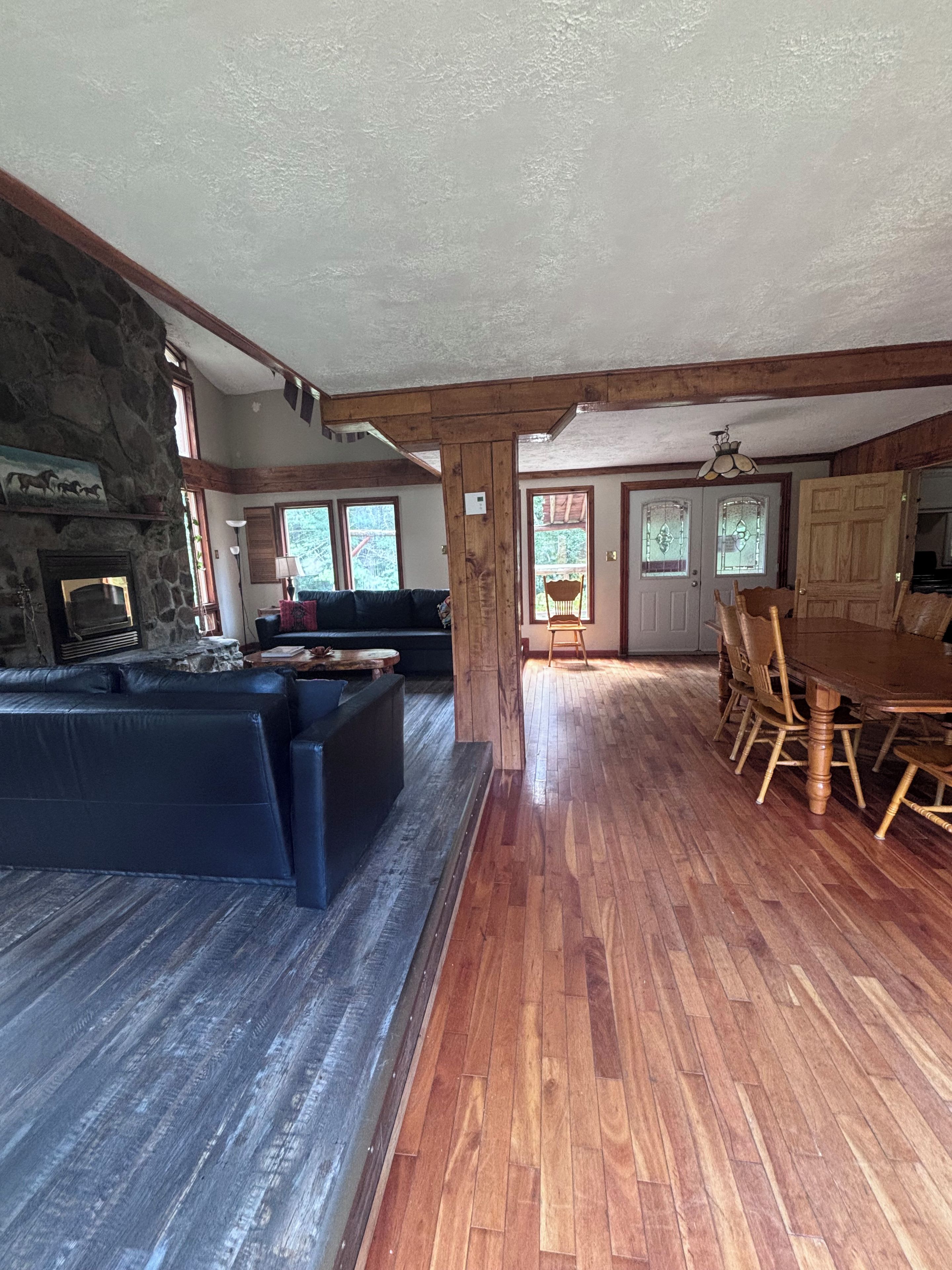 A spacious living area with a stone fireplace, a dark leather sofa, wooden flooring, and a dining table with chairs.