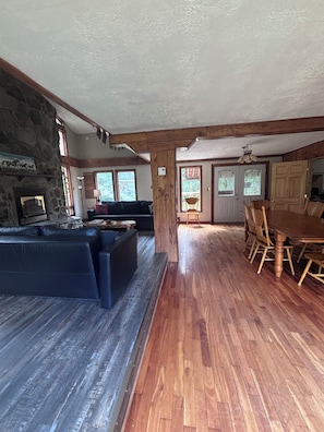 A spacious living area with a stone fireplace, a dark leather sofa, wooden flooring, and a dining table with chairs. - Rustic Ranch House Family Vacation Home (Alcove)
