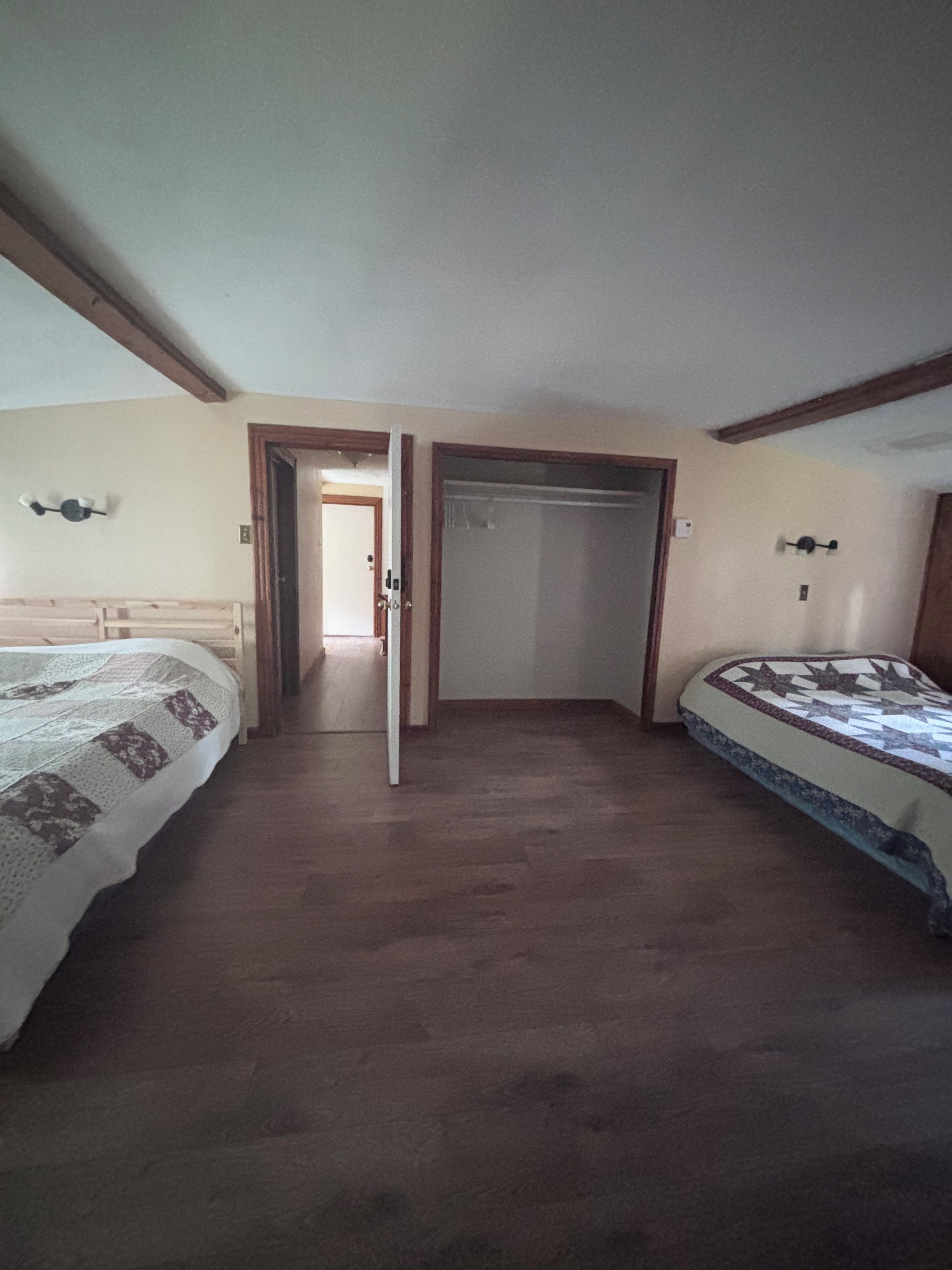 A room with two beds, a wooden floor, and a door leading to another room.