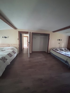 A room with two beds, a wooden floor, and a door leading to another room. - Rustic Ranch House Family Vacation Home (Alcove)
