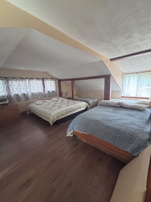 A bedroom with two beds, wooden flooring, a ceiling fan, and a window with curtains.