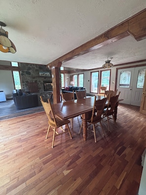 A spacious dining area with a wooden table and chairs, a stone fireplace, and large windows allowing natural light. - Rustic Ranch House Family Vacation Home (Alcove)