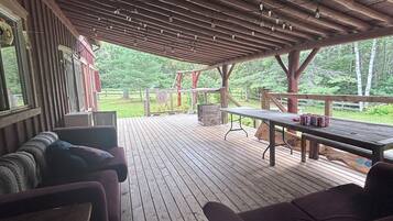 A covered outdoor seating area with wooden benches and a table, overlooking a grassy landscape.