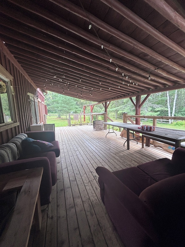 A covered outdoor seating area with wooden benches and a table, overlooking a grassy landscape. - Rustic Ranch House Family Vacation Home (Alcove)