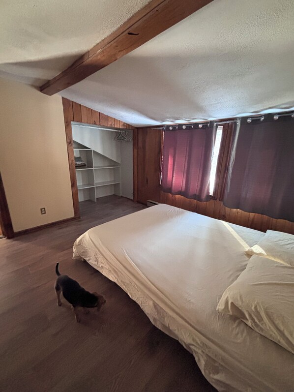 Un dormitori amb un llit gran, sòl de fusta, un armari amb prestatges i una escala que condueix a un nivell superior.