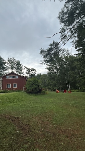 A grassy area with a red building and trees in the background. - Rustic Ranch House Family Vacation Home (Alcove)