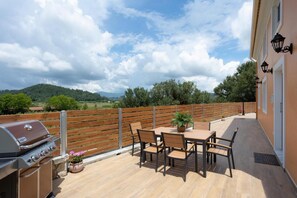 Eine Terrass mit Grill, Holztisch und Stühlen mit Blick auf eine hügelige Landschaft.