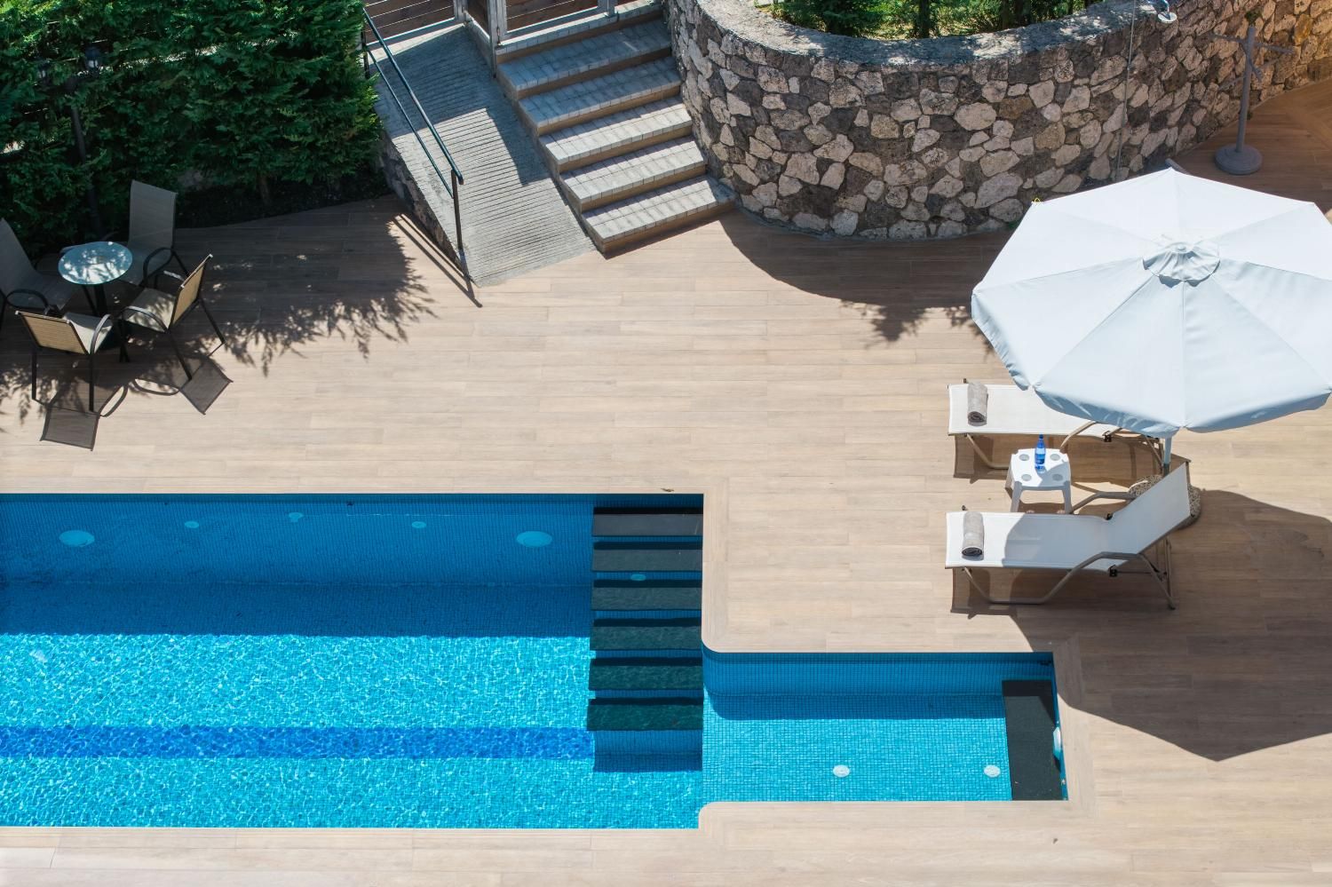 Ein Swimmingpool mit einer Steinsicht und Stufen, die zu einer Terrasse mit Gartenmöbeln führen.