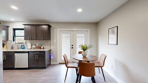 A modern kitchen with dark cabinets, a dishwasher, and a dining area with a round table and four chairs. - *NEW* Hullabaloo Hangout - 1.1 miles to Kyle Field! (College Station)