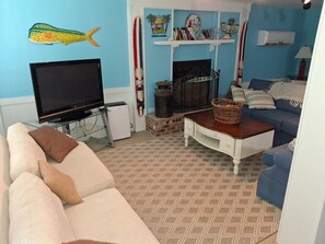 A living room with a television, a fireplace, and a blue sofa. - Canal Front Home on sought out street - Unique, Cozy and Ready for YOU! (Ocean Isle Beach)