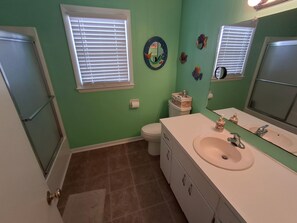 A bathroom with a toilet, sink, and shower. There are decorative fish on the wall and a mirror above the sink. - Canal Front Home on sought out street - Unique, Cozy and Ready for YOU! (Ocean Isle Beach)