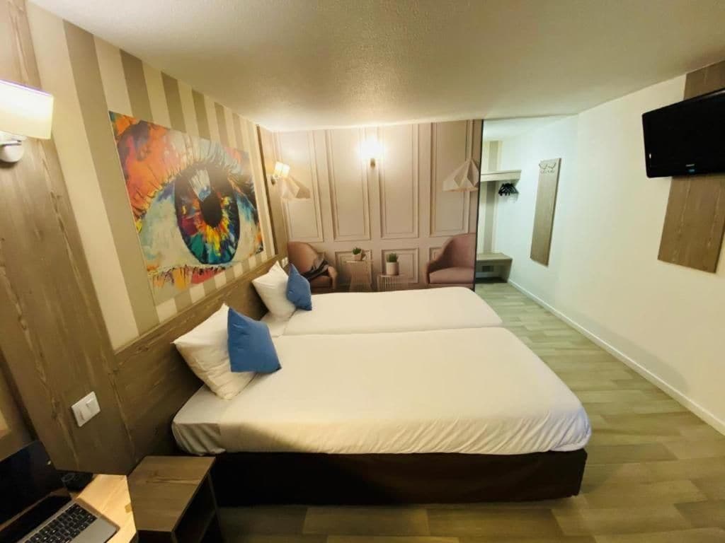 Een hotelkamer met een bed, een bureau met een laptop, een schilderij aan de muur en een aan de muur bevestigde televisie.