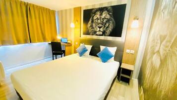 Une chambre d’hôtel avec un grand lit, un bureau avec un ordinateur et un tableau représentant un lion accroché au mur.
