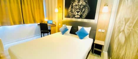 Een hotelkamer met een groot bed, een bureau met een computer en een schilderij van een leeuw aan de muur.