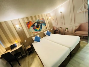 Una habitación de hotel con cama, escritorio, silla, lámpara y un cuadro en la pared.