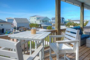 A wooden deck with white furniture, including a table and chairs, overlooking a residential area with houses. - Boozy Barradcuda: Ocean View, Pool, Game Room. Walk to Beach, Sleeps 16 (Oak Island)