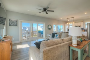 A spacious living room with a ceiling fan, a sofa, a coffee table, and a view of the outside. - Boozy Barradcuda: Ocean View, Pool, Game Room. Walk to Beach, Sleeps 16 (Oak Island)