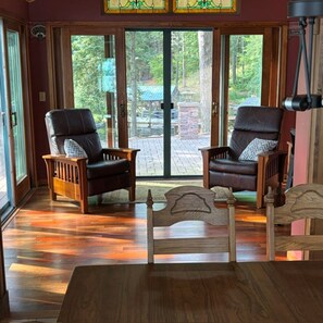Ein Zimmer mit zwei Ledersesseln, einem Holztisch und Blick durch eine Glastür in einen Außenbereich.
