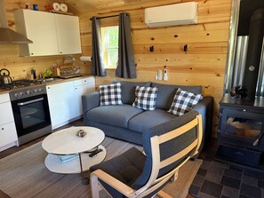 Un espace de vie compact comprenant un coin cuisine, un ensemble de canapés, une table à manger et un poêle à bois.
