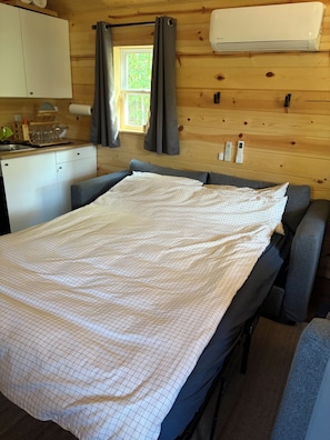 Una habitación pequeña con cama, una kitchenette y una ventana con cortinas.