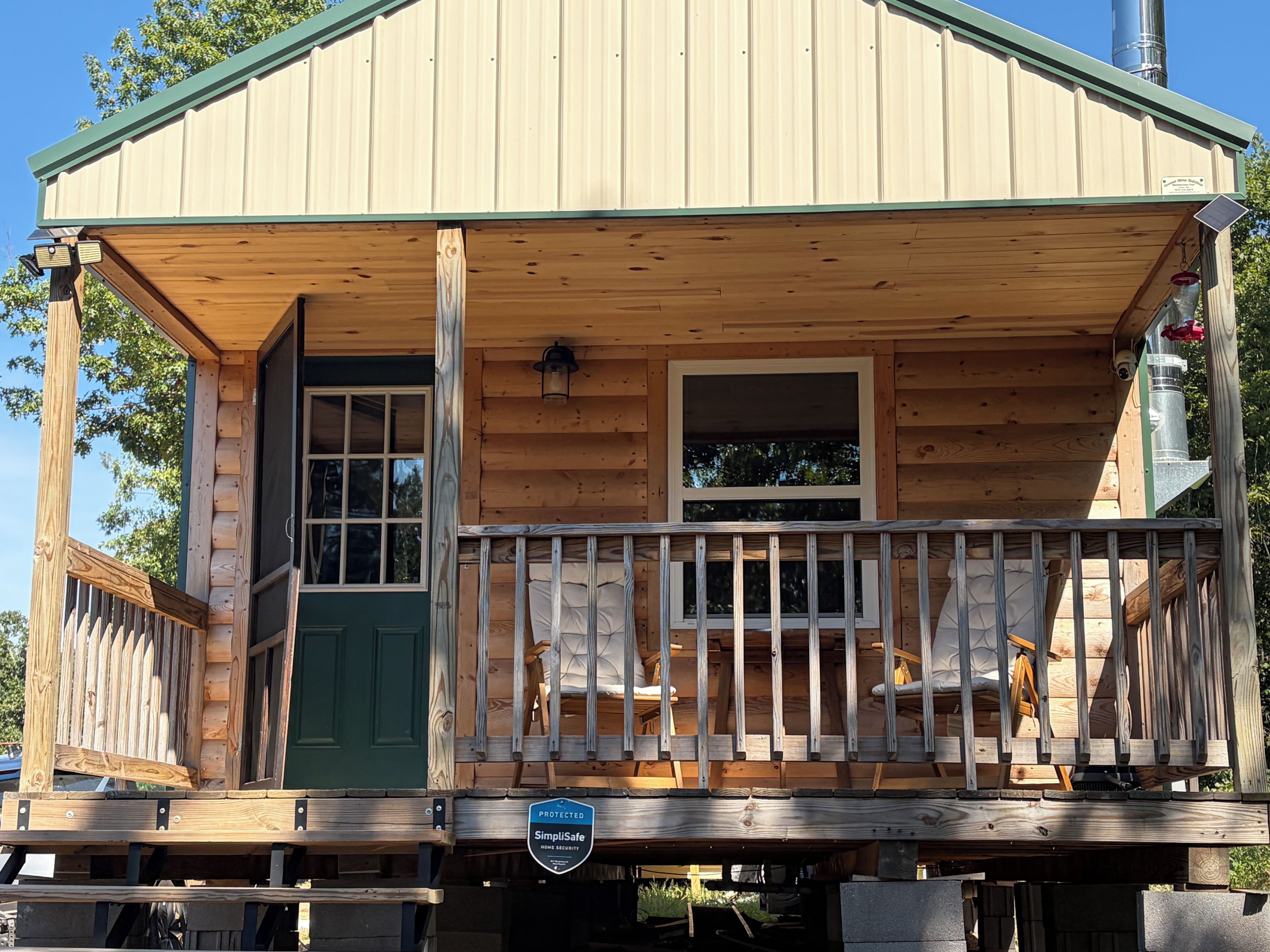 A wooden cabin with a porch, a green door, and a window.