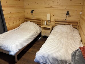 A wooden cabin room with two single beds, nightstands, and a lamp.