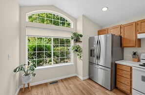 A kitchen with a stainless steel refrigerator, wooden cabinets, and a large window with a view of greenery. - Single-Level Beaverton Home | Sunroom & Garage (Beaverton)
