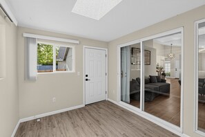 A spacious room with a large sliding glass door leading to a living area, a white door, and a window with blinds. - Single-Level Beaverton Home | Sunroom & Garage (Beaverton)