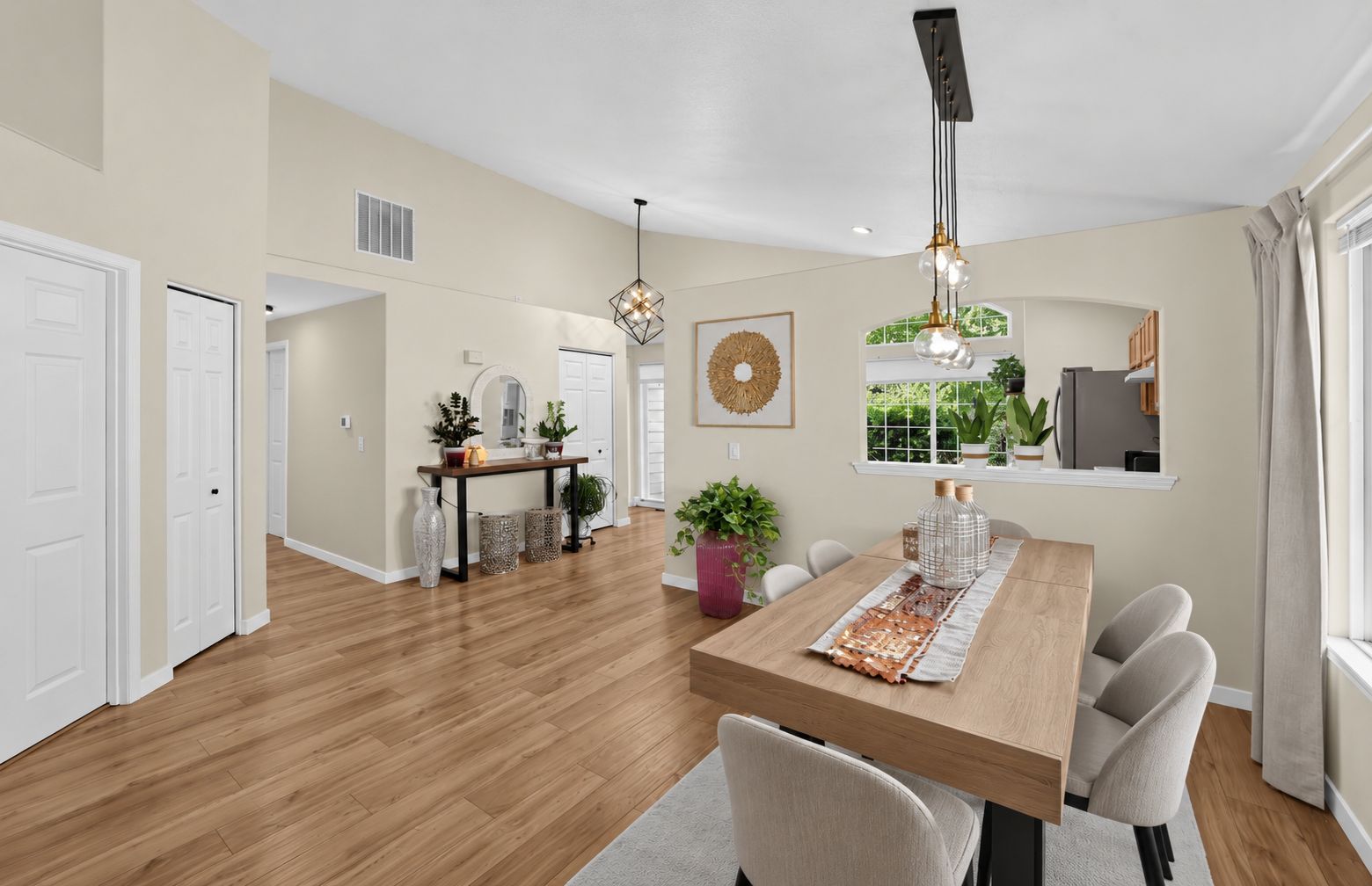 A spacious living area with a wooden floor, a dining table with chairs, a kitchen area, and a large window with curtains.