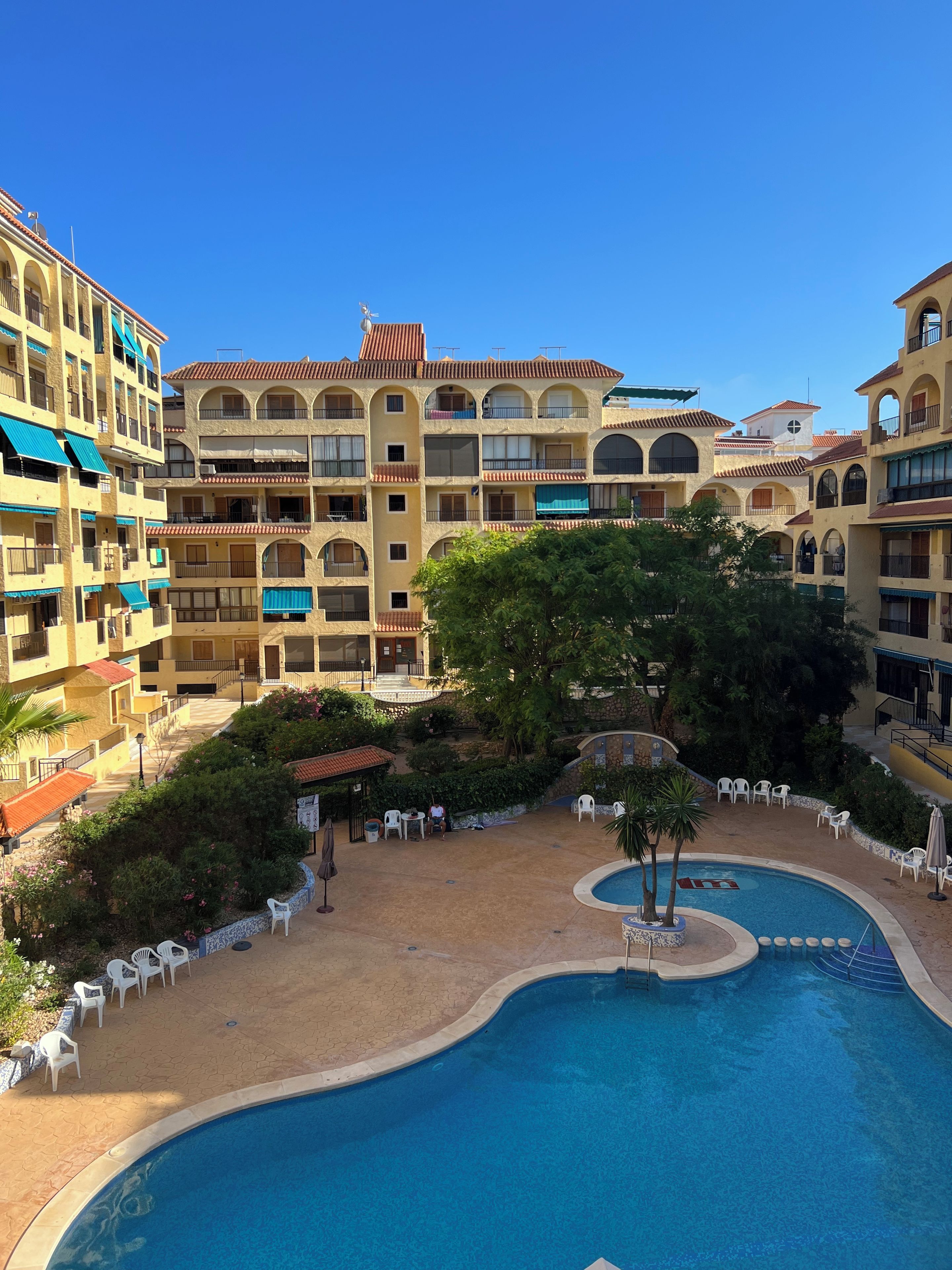 Une cour d’hôtel avec une piscine, des espaces de détente en plein air et des immeubles à plusieurs étages dotés de balcons.