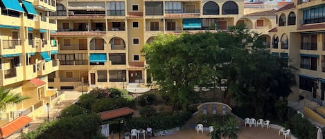 A hotel courtyard with a swimming pool, outdoor seating, and multi-story buildings with balconies.