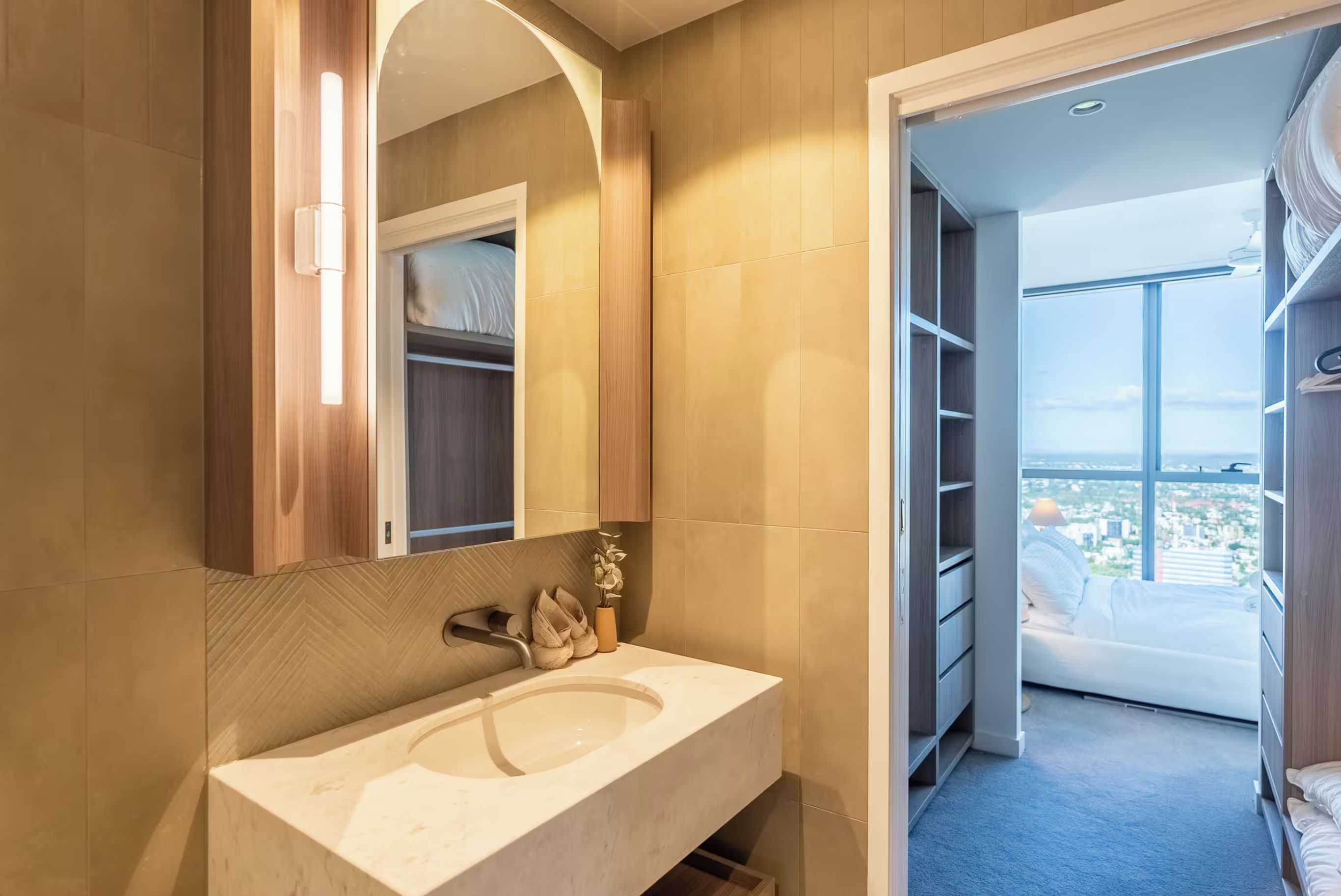 A modern bathroom with a large sink, a mirror, and a view of a balcony with a cityscape.