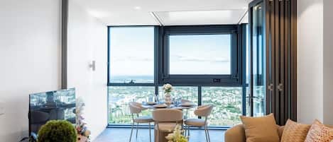 A modern living room with a dining area, large windows, and a city view.