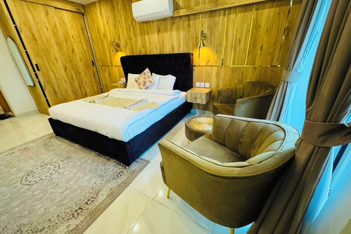 A bedroom with a bed, bedside table, lamp, and a chair.