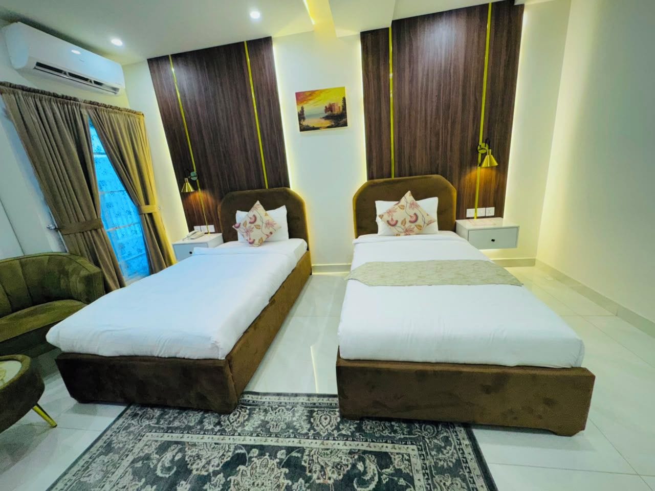 Habitación de hotel con dos camas, un sofá, un equipo de aire acondicionado y un cuadro en la pared.