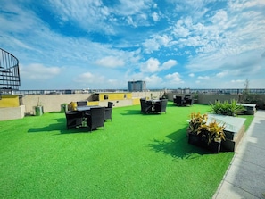 A rooftop terrace with artificial grass, outdoor furniture, and potted plants.