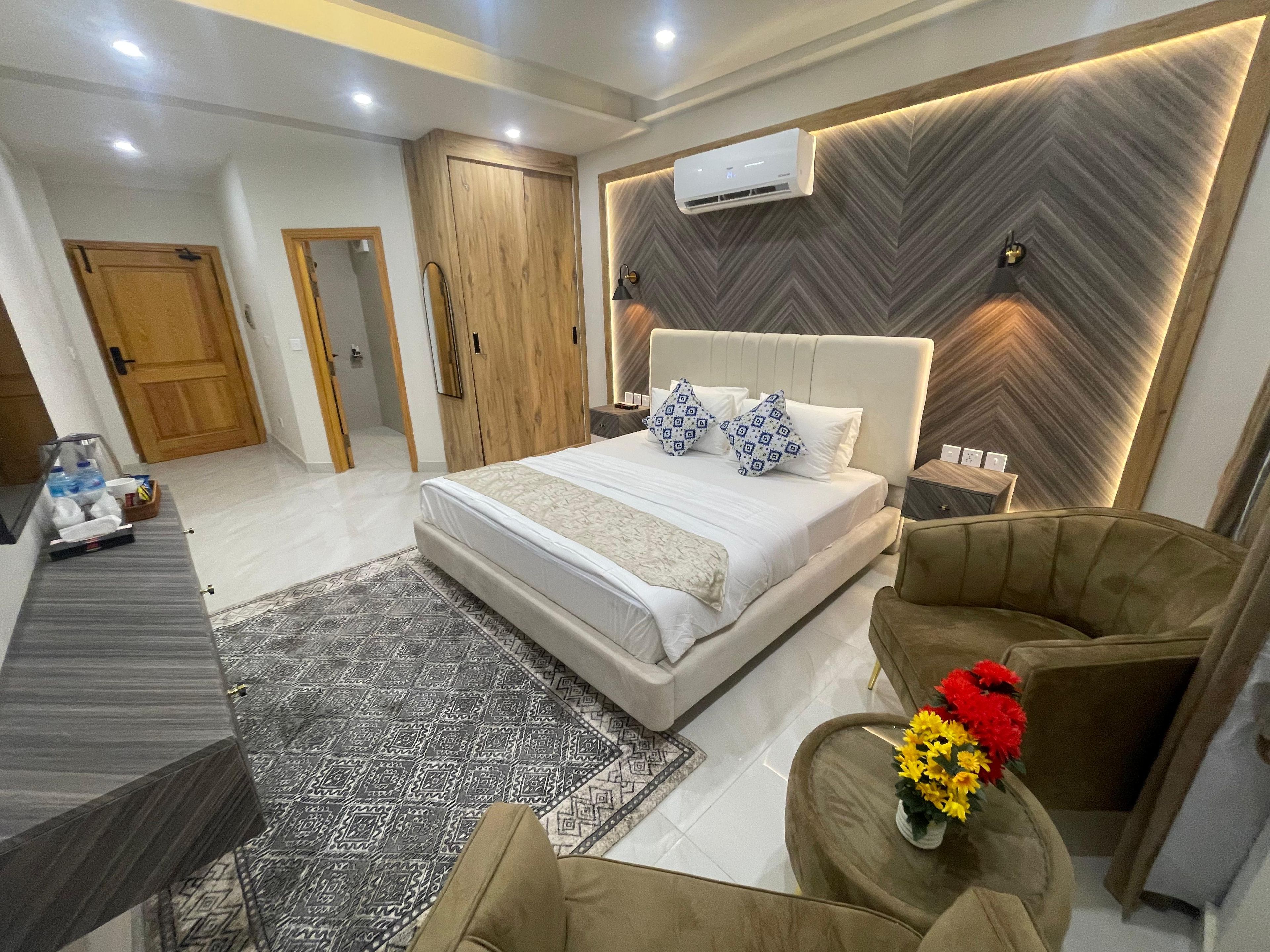A modern hotel room with a large bed, a sofa, a desk, and an air conditioning unit.