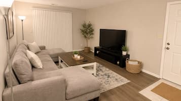 Uma sala de estar com sofá, mesa de centro, rack para TV e uma porta.