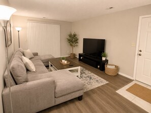 A living room with a sofa, a coffee table, a TV stand, and a door. - Enjoyable 2-bedroom apartment at St. Peters; Near STL (St. Peters)